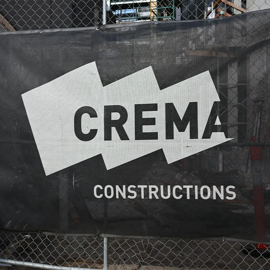 Black mesh printed banner with white ink logo installed on a chain-link construction fence
