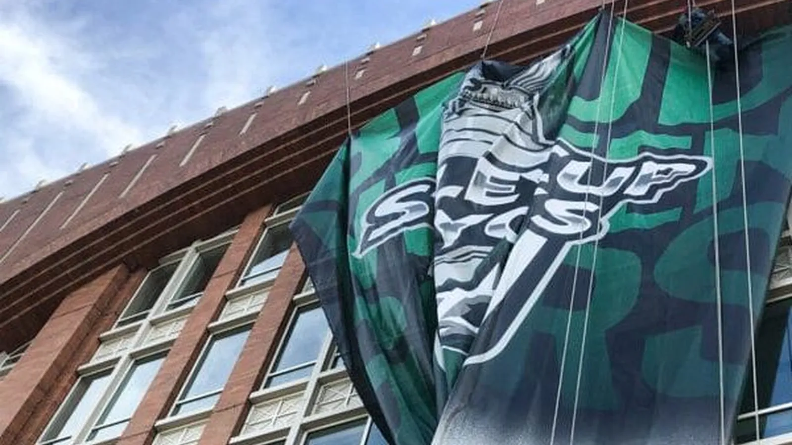 Large building banner being installed on a storefront facade in Dallas by Positive Marketing USA