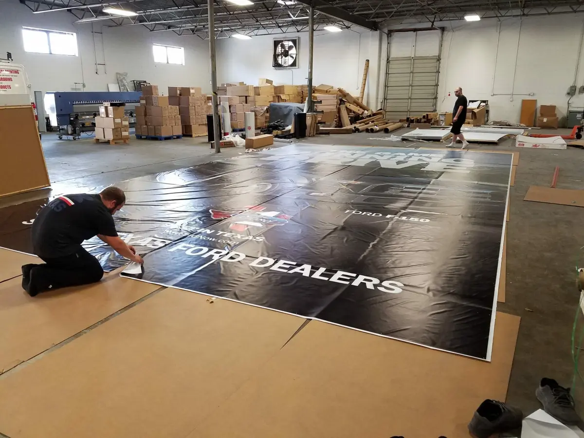 Production team finishing a building-size Texas Ford Dealers banner in a Dallas large format printing facility