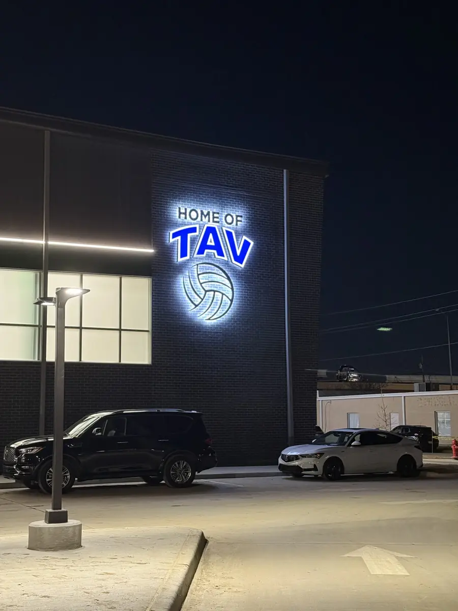 Halo-lit Home of TAV building sign with volleyball logo glowing on brick wall in Dallas